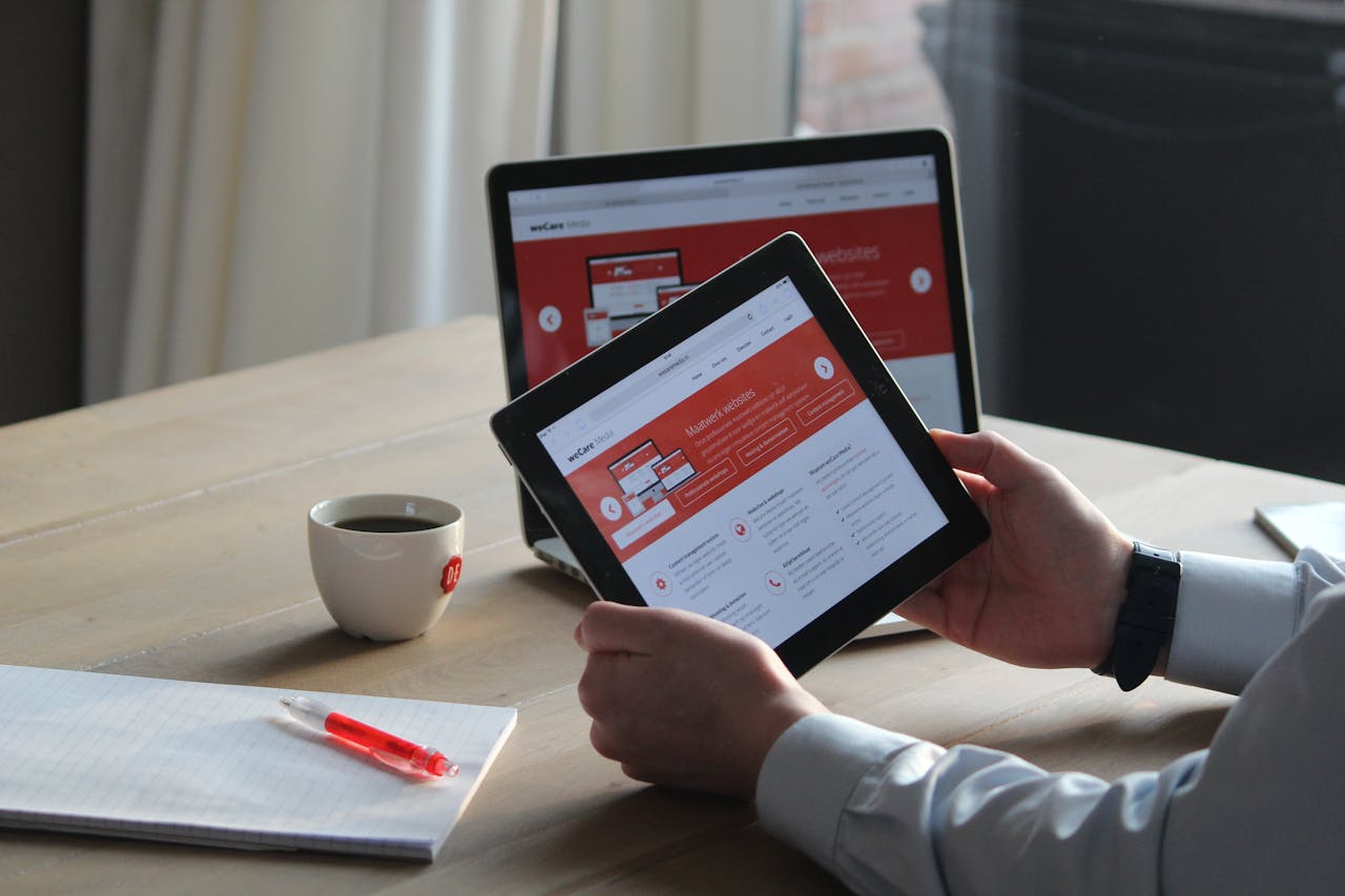 home-img Business professional using a tablet and laptop with a hot drink, focusing on digital content review.